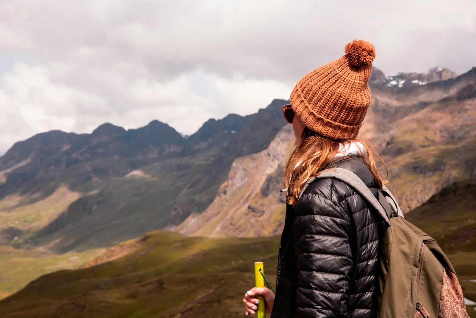 Viajera de espaldas con gorro terracota mirando las montañas de los Andes cerca de Cusco